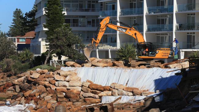 A bulldozer moves large bolders to build a temporary wall as protection against further swell surges at Collaroy. Picture: Toby Zerna