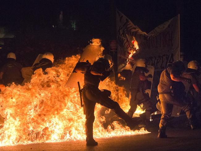 Riot police officers run away from the fire as anti-austerity protesters throw petrol bombs.