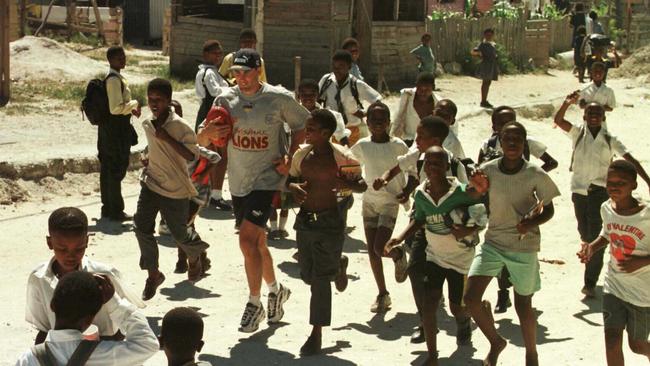 Brisbane Lions’ Marcus Ashcroft takes some young children on a run through Nyanga township in Cape Town, South Africa during a football clinic for the AFL Ansett Cup visit in 1998. Picture: Tony/Feder/Sporting Pix.