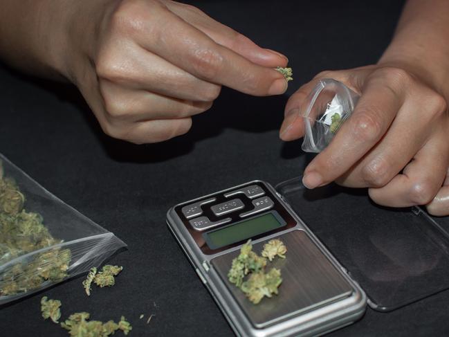 Sell and buy marijuana or drugs. Person weighing and preparing a bag of weed to sell on black table.