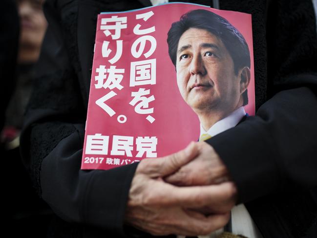 In this picture taken on October 18, 2017, a man holds an electoral leaflet of Japan's Prime Minister and ruling Liberal Democratic Party (LDP) president Shinzo Abe during an election campaign in Saitama. Japan's Shinzo Abe, seeking a fresh term in October 22nd election, is seen as a pragmatic and canny diplomat who has cozied up to Donald Trump and Vladimir Putin while pushing a nationalist agenda at home. Groomed for power from birth, the 63-year-old is often viewed as arrogant but has also shown a self-deprecating sense of humour, dressing up as video game icon Super Mario as the Rio Olympics closed to give a zany preview of Tokyo 2020. / AFP PHOTO / Behrouz MEHRI / TO GO WITH ELECTION PROFILE 