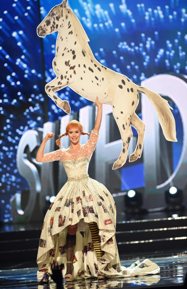 woman in spotted dress and red-braid wig, brandishing a large paper horse overhead