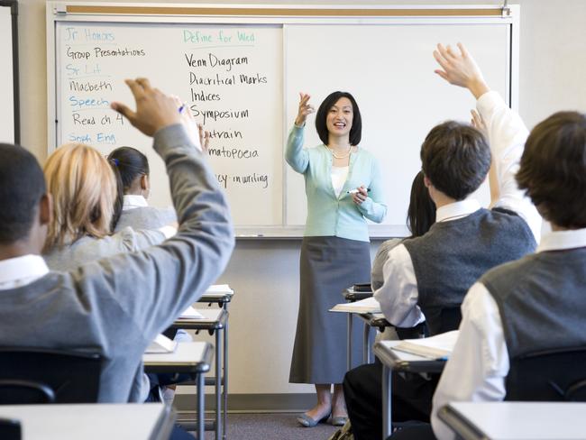 School children (14-18) raising hands in class