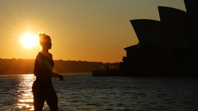 A person runs past the Sydney Opera House as the sun rises over Sydney Harbour. Clear blue skies in Sydney today. Picture: NewsWire / Damian Shaw