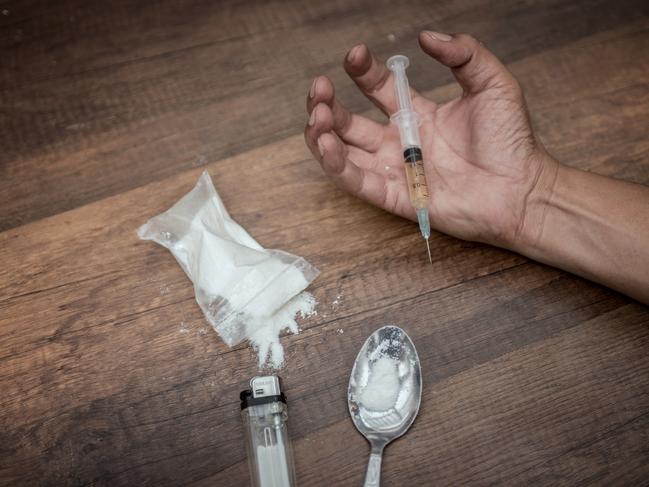 Unconscious drug addict hands lying on grungy concrete floor with pills, syringe, cooked heroine. Dangers of drug addict and abuse concept. International Day against Drug Abuse.