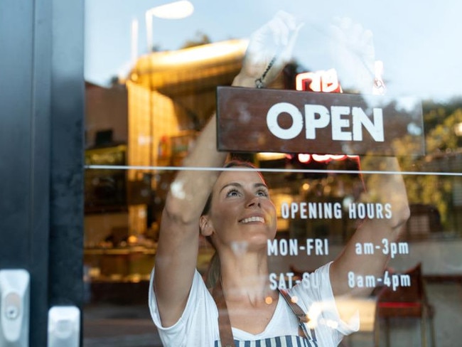 Portrait of a happy business owner hanging an open sign on the door at a cafe and smiling - food and drinks concepts