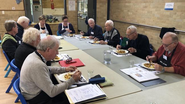 Participants, and their two volunteer instructors, in a Men's Kitchen Northern Beaches cooking skills session, enjoy the lunch they prepared at the Forestville Community Hall on Friday. Picture: Jim O'Rourke