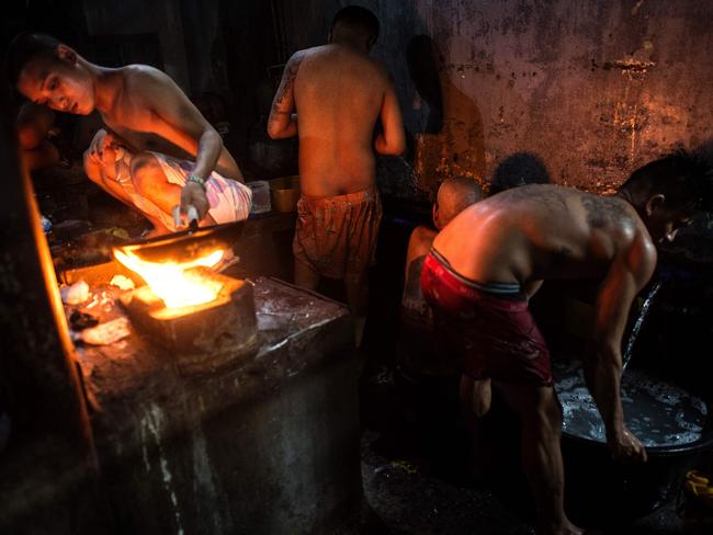 An inmate cooks his dinner as other detainees take a bath nearby. Picture: Ayee Macaraig