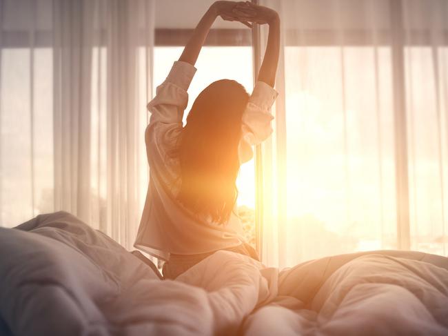 Happy woman stretching in bed after waking up.