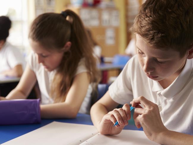 Two kids working at their desks in primary school, close up