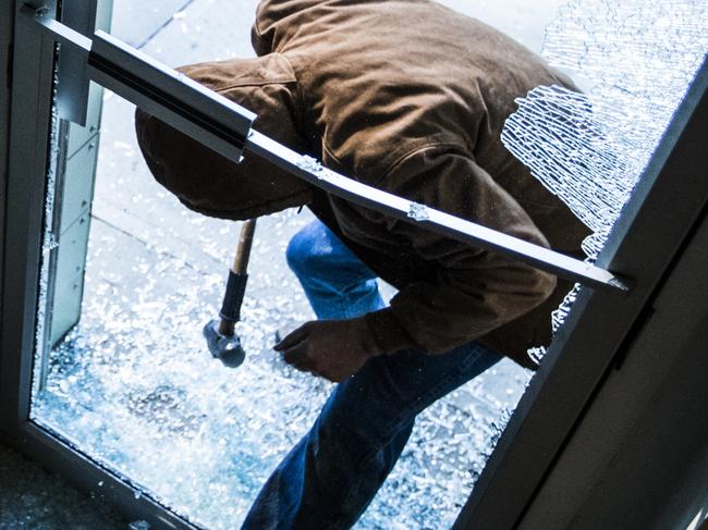 A robber using a sledgehammer to break the glass of a retail store.