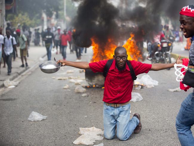 A demonstrator kneels in front of a burning barricade holding a bowl and spoon to show his hunger, during a protest to demand the resignation of President Jovenel Moise in Port-au-Prince, Haiti. Picture: AP