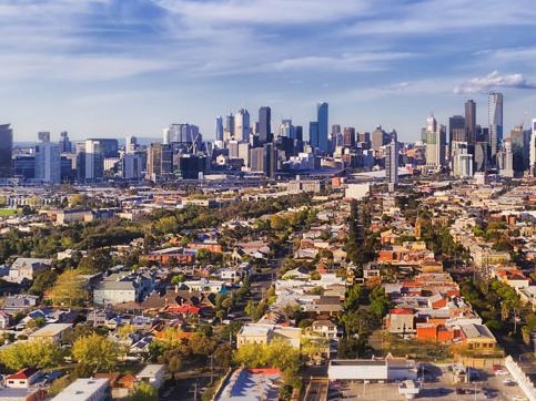 Aerial view of Melbourne city CBD high-rise towers from Port Melbourne and Southbank above residential suburb house roofs and local streets, roads, cars and parks.