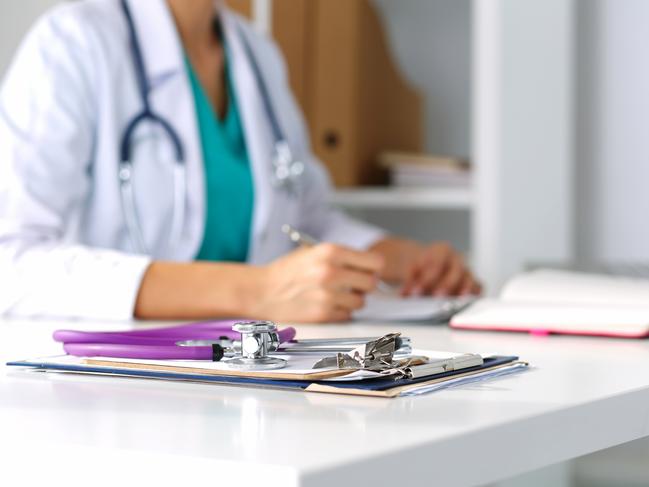 Stethoscope head lying on medical forms on clipboards closeup while medicine doctor working in background and analysing a health insurance policy. Picture: iStock.