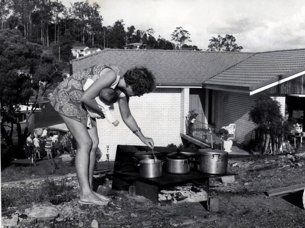 Mrs Leonie Grice holding baby Melissa, cooking over a wood fire on a barbecue plate at Jindalee after power loss.
