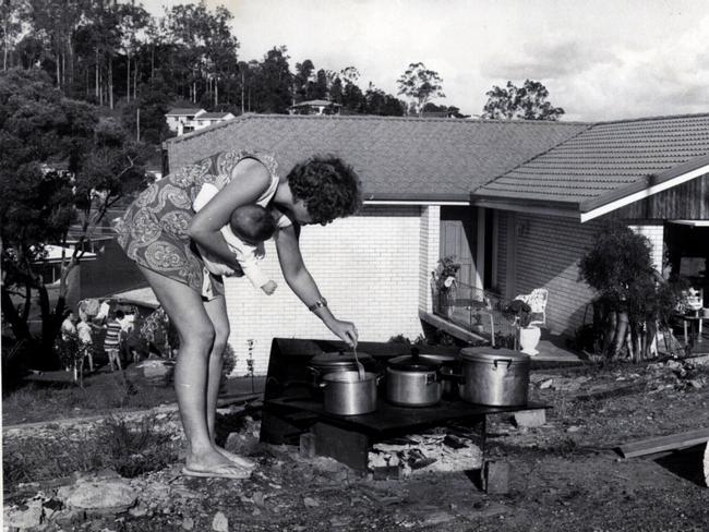 Mrs Leonie Grice holding baby Melissa, cooking over a wood fire on a barbecue plate at Jindalee after power loss.
