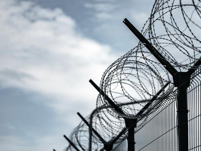 Barbed Wire Fence. Prison or border fence with razor wire against dark sky. Security concept