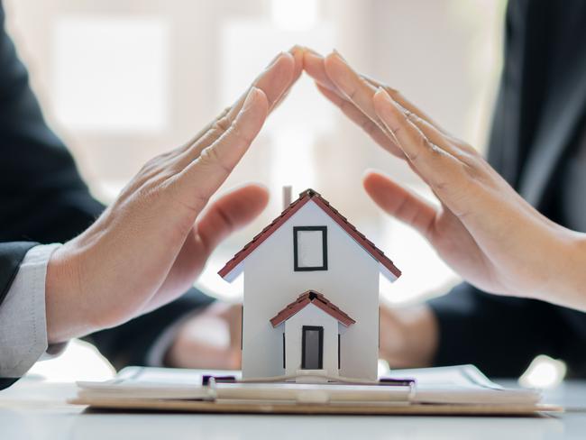 A young woman and a man use both hands to protect the house on the table. home insurance concept; housing, home loan shield, mortgage defence generic