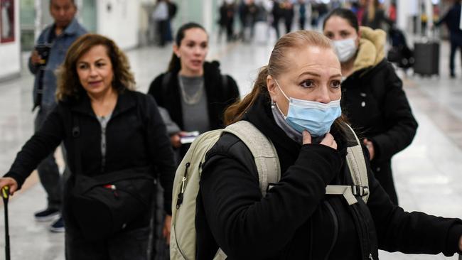 Airport passengers wearing protective masks ... Australian health experts are recommending people who have been in contact with any coronavirus cases should be isolated in their home for 14 days following exposure. Picture: AFP