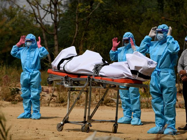 Relatives wearing personal protective equipment offer funeral prayers in front of the body of a COVID-19 before burial at a graveyard in New Delhi. Picture: AFP