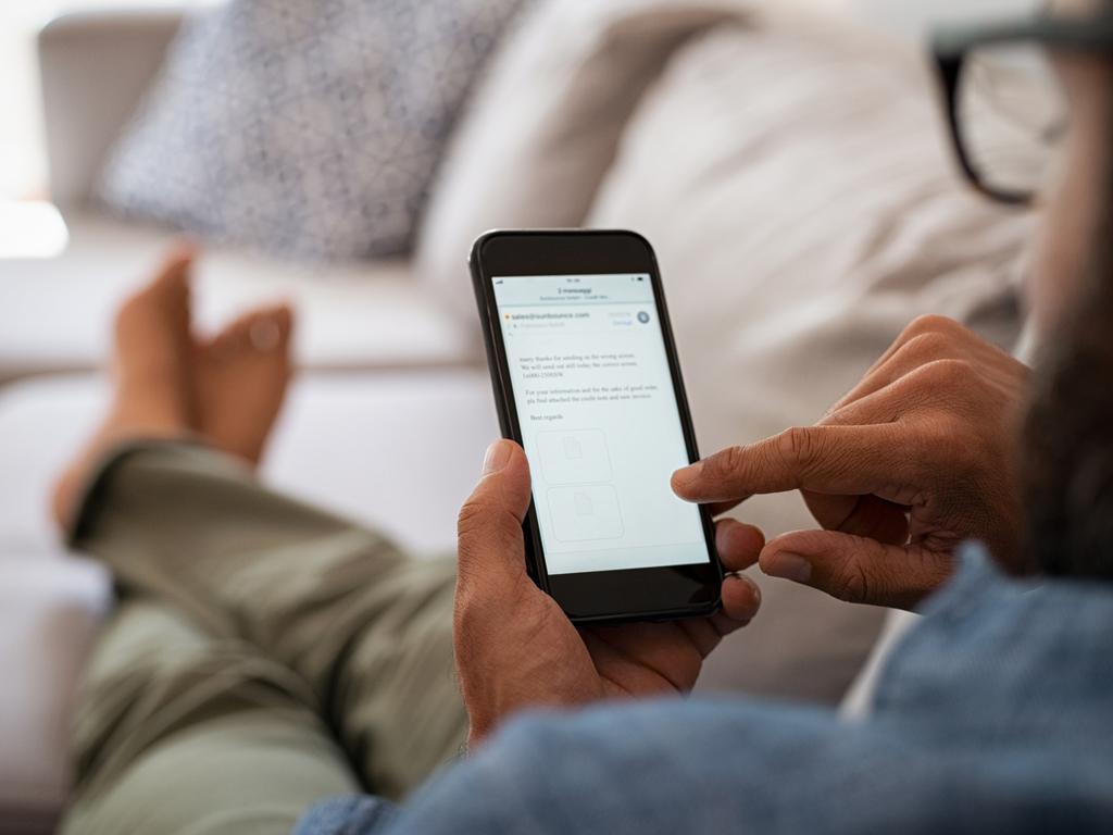 Closeup of a man hand holding cellphone with internet browser on screen. Man with spectacles relaxing sitting on couch while looking at mobile phone. Closeup of mature latin man using smartphone to checking email at home.