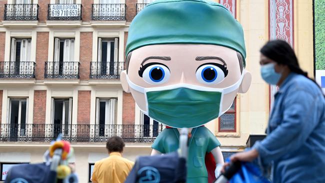 People wearing face masks walk on September 24, 2020 by a 6 meters high statue depecting a "Superhealthworker"  installed in Madrid to pay tribute to the heroes who fight against coronavirus. (Photo by Gabriel BOUYS / AFP)