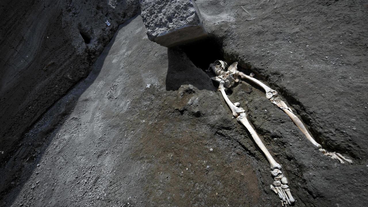 The legs of a skeleton emerge from the ground beneath a large rock believed to have crushed the victim's bust during the eruption of Mt. Vesuvius in A.D. 79, which destroyed the ancient town of Pompeii, at Pompeii's archeological site, near Naples, on Tuesday, May 29, 2018. The skeleton was found during recent excavations and is believed to be of a 35-year-old man with a limp who was hit by a pyroclastic cloud during the eruption. (Ciro Fusco/ANSA via AP)