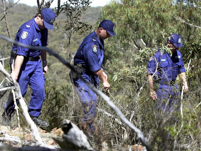 Police officers searching bushland for a missing person.