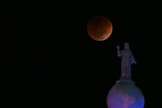 This multiple exposure picture shows the blood moon during a total lunar eclipse seen past the Saviour of the World monument in Salvador del Mundo Square, in San Salvador. Picture: Marvin RECINOS / AFP