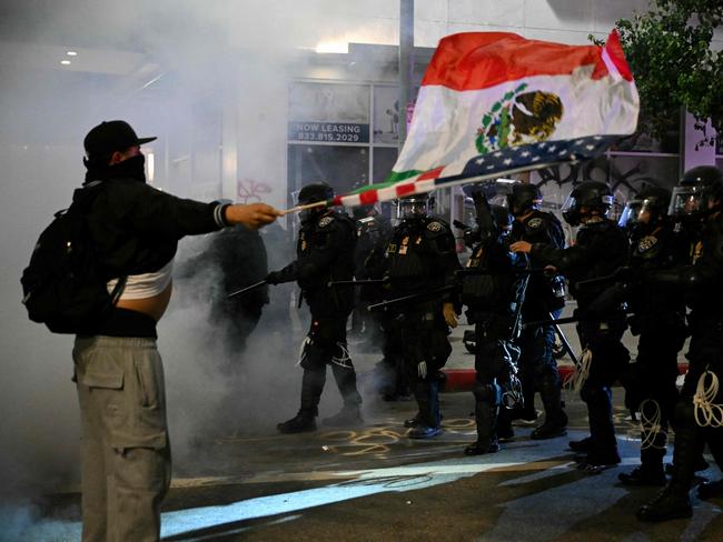 A protester waves a combination Mexican-US flag in front of police in riot gear during a protest in response to federal immigration operations in the Little Tokyo neighborhood of downtown Los Angeles, on June 9, 2025. President Donald Trump's administration said on June 9 that it was sending 700 US Marines and thousands more National Guard troops to Los Angeles, sparking a furious response from California's governor over the 