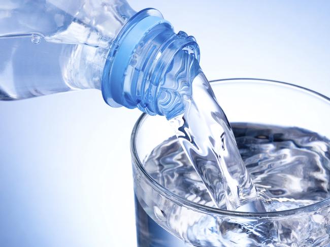 Close-up Pouring glass of water from a plastic bottle on blue background
