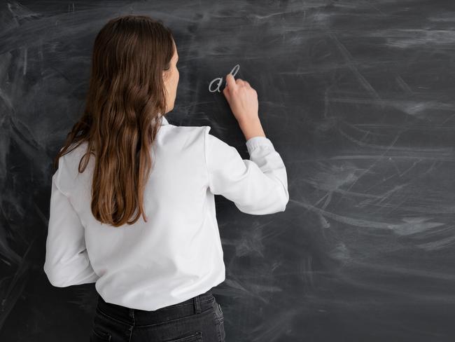 student woman or teacher in the class writes math formulas in chalk on a black chalkboard. young girl stands with her back to the camera. Back to school. Education concept. Banner. Place for your text