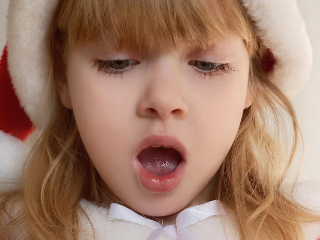 A pretty young girl in a Christmas outfit singing Christmas carols or with an expression of surprise on her face (shallow DOF with focus of face).