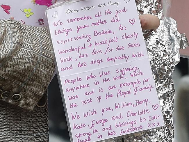 Britain's Prince William takes flowers and notes from members of the public which he then placed amongst the floral and pictorial tributes to his late mother Princess Diana placed on the gates of Kensington Palace, London, Wednesday, Aug. 30, 2017. Princes William and Harry paid tribute to their mother, Princess Diana, on the eve of the 20th anniversary of her death by visiting the Sunken Garden to honor Diana's work with charities. (AP Photo/Kirsty Wigglesworth)