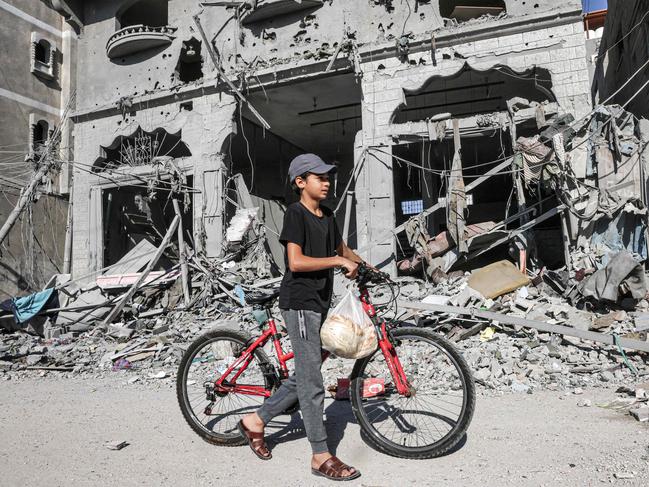 A Palestinian child carries bread as he pushes his bike amid the rubble of buildings destroyed in an Israeli air strike in Rafah, on the southern Gaza Strip. (Photo by SAID KHATIB / AFP)