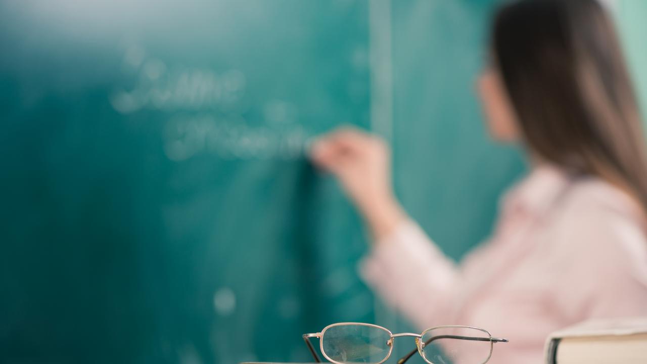 glasses and books at the classroom table while teacher writing on a blackboard