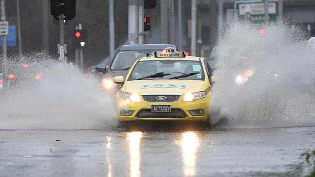 Cars pass through the water covered intersection of Racecourse and Flemington Rd in Melbourne. Picture: James Ross.