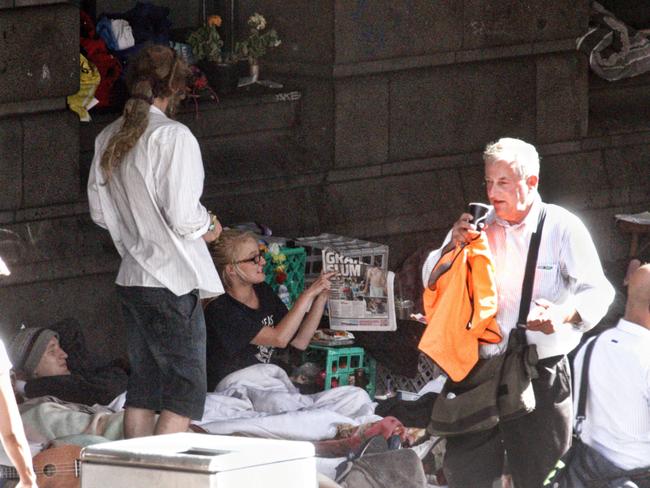 Homeless people camped outside Flinders St station as people walk past. Picture: Mark Stewart