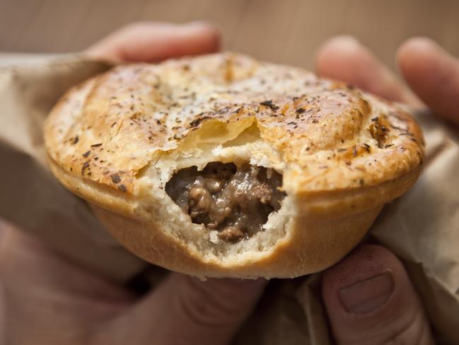 Close-up of a man's hands holding an Australian meat pie with a bite taken out of it.