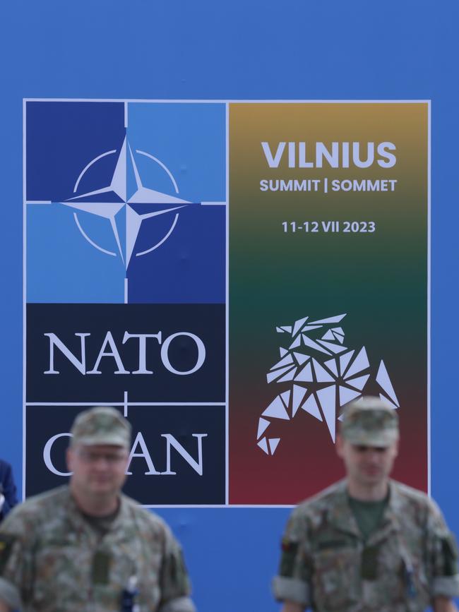 Soldiers walk past a poster at the NATO summit venue.