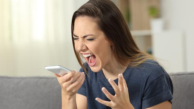 Furious woman shouting to smart phone sitting on a couch in the living room at home; Customer service frustration generic