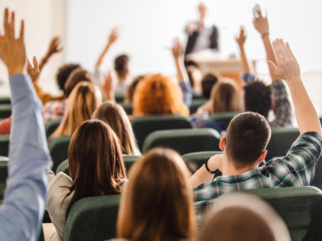 Back view of college students raising their arms on a class at lecture hall.