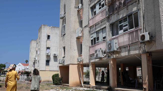 Residents walk next to a building damaged by a rocket fired from Lebanon in the Israeli coastal town of Acre. Picture: AFP.