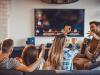 Happy roommates having fun while spending their time together in the living room. Two of them are watching TV while other two are dancing.