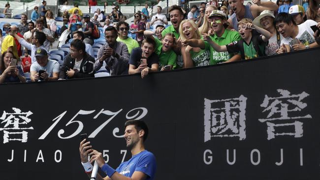 Novak Djokovic takes a selfie with spectators today as he practices on Rod Laver Arena ahead of his men's singles final against Spain's Rafael Nadal. Picture: Kin Cheung/AP