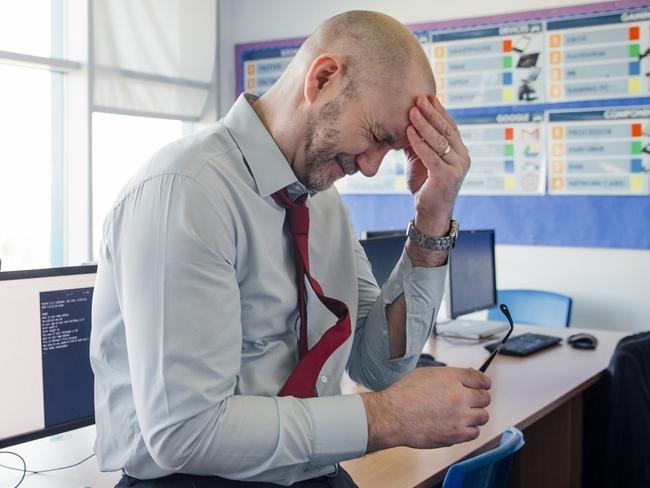 Stressed, concerned teacher sits on the edge of a desk in an empty classroom, schools, upset. Istock