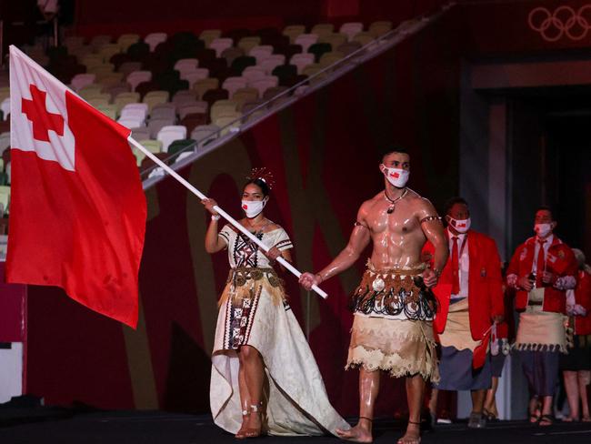 Tonga's flag bearers Malia Paseka (L) and Pita Taufatofua (C) leading the delegation during the Tokyo 2020 Olympic Games opening ceremony's parade. Mr Taufatofua is praying for news of his father, who he has not heard from since a devastating tsunami hit the island. Picture: Hannah McKay/AFP