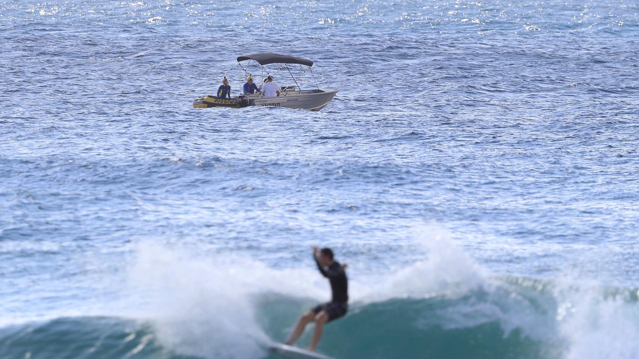 A surfer riding a wave with the rescue scene in the background. Photo: Adam Head