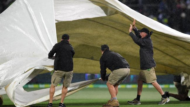 Ground staff struggle to lay the covers as the rain and wind arrives in Adelaide.