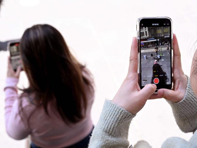 Young people look at their phone in Melbourne on November 28, 2024 as Australia looks to ban children under 16 from social media with claims social media platforms have been tarnished by cyberbullying, the spread of illegal content, and election-meddling claims. Australia is among the vanguard of nations trying to clean up social media, and the age limit legislation will make it among the world's strictest measures aimed at children. (Photo by William WEST / AFP)